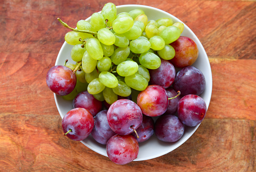 green grapes and plums in a plate on a wooden board, concept of fresh fruits and healthy food
