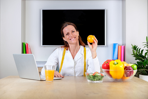 Portrait of smiling nutritionist holding a orange. Dietitian woman with big smile and showing to orange. Vitamins and healthy diet concept