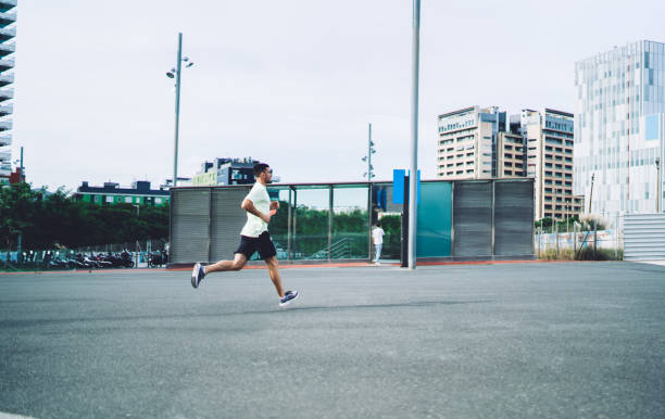 マラソンの準備をしている決然とした男性アスリートの側面図は、都市都市部で有酸素運動の朝のトレーニングを受け、スポーツウェアを着たやる気のある男性が健康的なライフスタイルを� - marathon sport sports training city street ストックフォトと画像