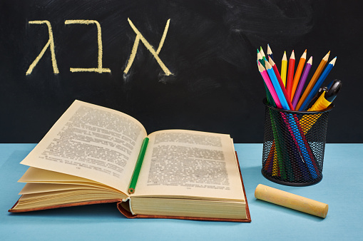 ABC letters written in Hebrew. Concept of education or back to school. An open book, a set of colored pencils.