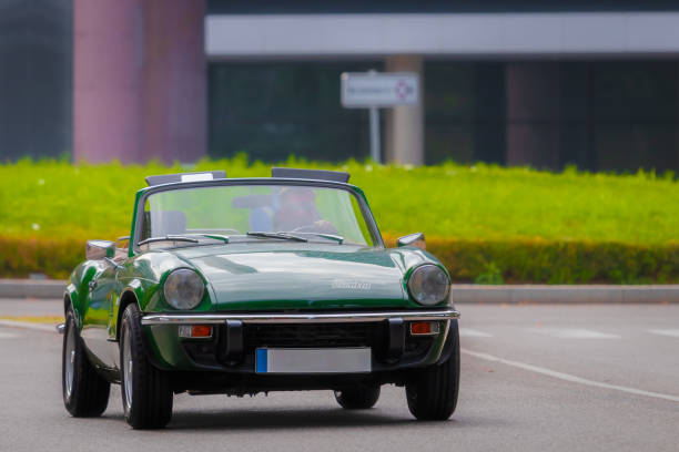 Classic bright red Triumph Spitfire roadster driving down old city street at dusk. Oldtimer travel, iconic vintage style, and the romantic mood of summer evening town. Subotica, Serbia, 05 July 2025