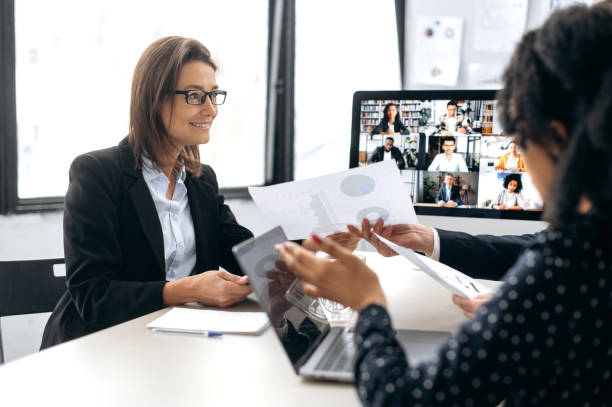 istock Two influential successful business colleagues, working together in modern office, study financial documents, talking with partners by online video conference by computer, discuss business strategy 1415987352