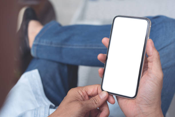 istock Mockup image blank white screen cell phone. Man hand holding, using mobile relax on sofa at home. background empty space for advertise text 1415995352