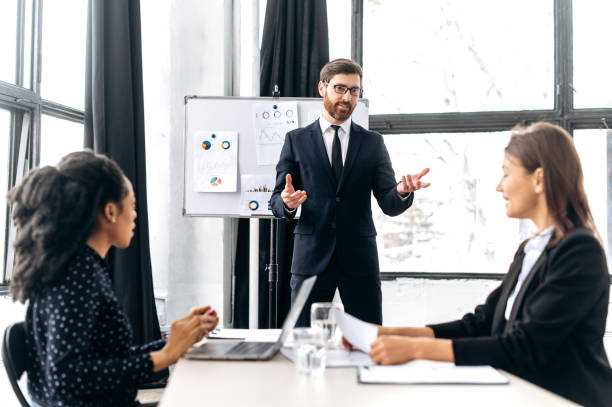 istock Influential Caucasian attractive male boss, holding group brainstorm, discussing ideas for a new business project, makes a business plan presentation to his female partners. Teamwork, collaboration 1415996140