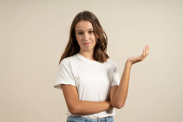 cute latin teen girl open her hands palm up holding something. surprised happy girl on isolated beige background. european teenager of about 13 years - 12 13 years fotos imagens e fotografias de stock