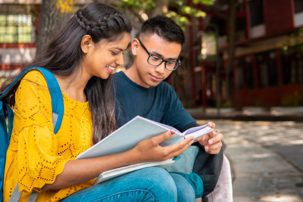 Multiethnic college student friends studying together at campus. University student friends from different ethnicities holding a book and discussing about studies at a campus. boy and girl reading stock pictures, royalty-free photos & images