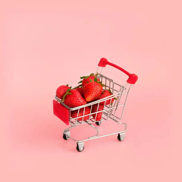 Fresh red strawberry in shopping card on pink background. Online shopping and Valentines Day minimalistic concept. Black Fridays sales banner. Healthy, organic, vegan food
