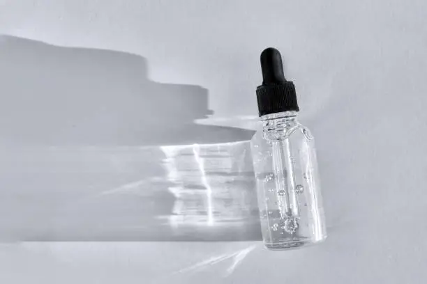 Transparent glass dropper bottle with air bubbles on gray background. Pipette with fluid hyaluronic acid, serum, retinol or oil. Cosmetics and healthcare concept. Flat lay. Luxury beauty product