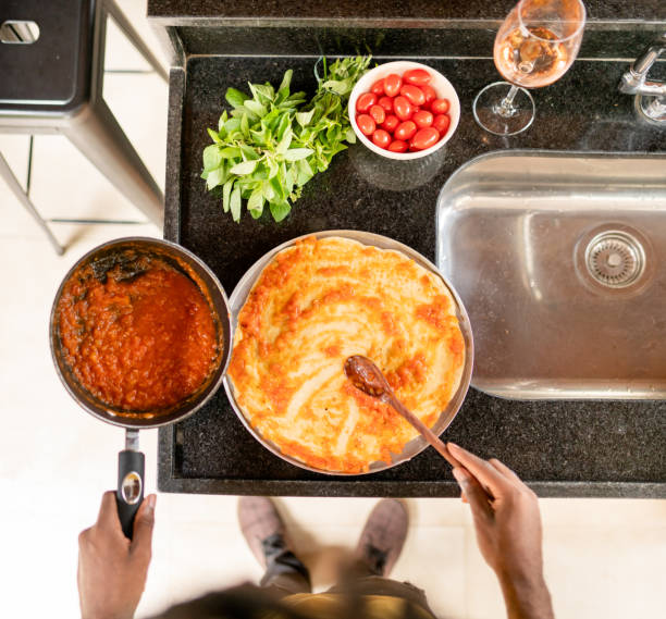 Close-up of a man putting sauce on a pizza base at a counter in a kitchen at home