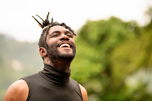 Stylish young man with dreads and a beard standing outside in the summer and laughing