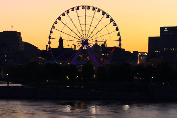 Long exposure of Montreal Grand Ferris Wheel in Old Port at sunset. Reflections of sun rays on Saint Laurent river with a background of cloudy blue sky stock photo