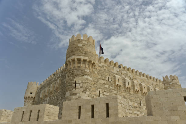 Citadel of Qaitbay, Alexandria, Egypt with the Egyptian flag on top and a background of blue cloudy sky. The Fort of Qaitbay is a 15th-century defensive fortress located on the Mediterranean sea coast stock photo