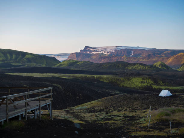 アイスランドのボトナーキャンプ場にある木製のテラスと白いテント、ラウガベグルハイキングコース、ミュルダルショクル氷河の景色を望む火山風景の緑の谷。早朝日の出ピンクライト - camping outdoors iceland red ストックフォトと画像
