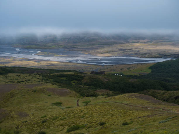 View from top of Valahnukur mountain on landscape of green valley of Thorsmork with volcano huts camp site, sharp green rocks, river Krossa delta and green forest. Foggy summer day, Highlands of Iceland. vista desde la cima de la montaña valahnukur en el paisaje del valle verde de thorsmork con cabañas volcánicas en el campamento, rocas verdes afiladas, delta del río krossa y bosque verde. día de verano con niebla, tierras altas de islandia