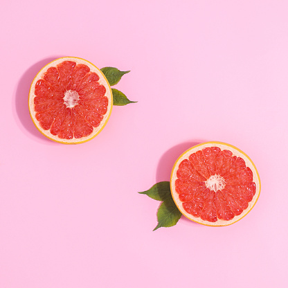 two half pieces of grapefruit with green leaves on pastel pink background. Creative copy space flat lay