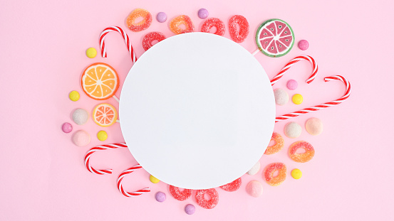 White paper copy space with candies around on pastel pink background. Flat lay