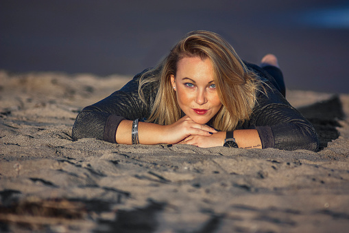 Girl lying on the sand of the beach with smiling expression while looking at the resume point.