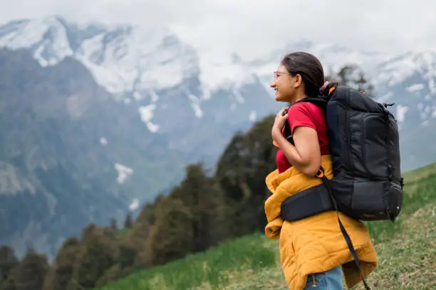 Teenager Indian girl hiking on mountain with backpack in Manali, Himachal Pradesh, India. Female hiker enjoying idyllic view of Himalayan mountain range. Travel and adventure activity