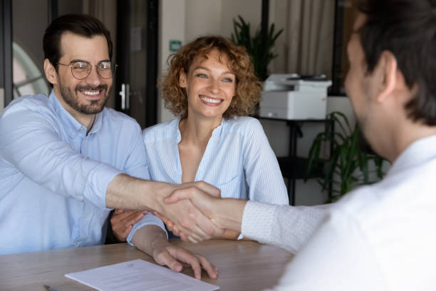 Young family couple shaking hands with hispanic lawyer. Joyful beautiful young family couple shaking hands with hispanic lawyer or broker, feeling thankful for professional consultation. Happy clients making agreement with real estate agent at office meeting. independence document agreement contract stock pictures, royalty-free photos & images