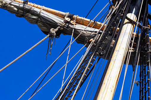 Vintage old sailing ship mast with clear blue sky background. Sail and mast with rigging and guys of an old sailing ship