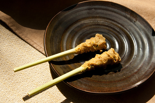 Two Balinese Chicken Satay on Lemongrass skewers served in ceramic plate on dining table, Bali Indonesia.