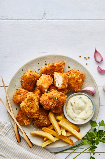 Chicken nuggets in a plate, with white sauce, garlic and lemon, served on a white wooden restaurant or home table, top view with copy space