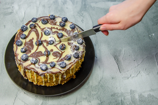 woman's hand cuts a large homemade cake with a knife on the background of a concrete tabletop