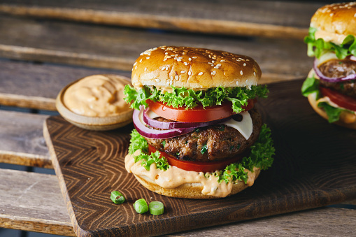 Colorful and tasty burger on a homemade wooden cutting board and dark background