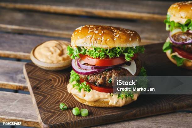 Cheeseburger On A Homemade Wooden Cutting Board With A Dark Background Stock Photo - Download Image Now