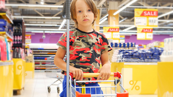 A little boy rolls a small shopping trolley in a shopping mall