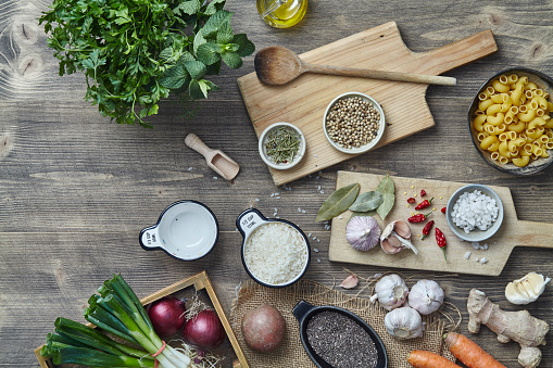 Fresh and dry ingredients, vegetables, herbs, spices and seasoning on a kitchen wooden table top, top view with a free space for copy