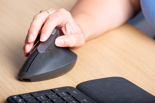 A modern laptop and a vertical mouse in a panoramic shot. An ergonomic vertical mouse is used by a man in a shirt to prevent carpal tunnel syndrome. Designers, gamer, and medical suggestions.