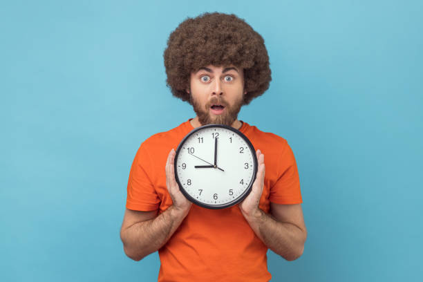 istock Man being late, holding in hand wall watch, deadline, punctuality, looking at camera with open mouth 1416037621