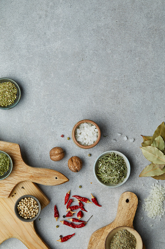 Seasoning (herbs and spices) on a wooden cutting board, on a modern gray kitchen table top, background ceramic texture for vegan or vegetarian food preparation, top view with a free space for copy