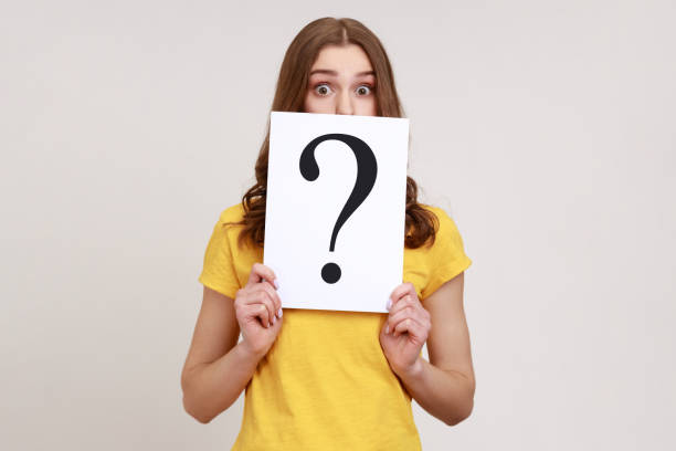young surprised female holding white billboard with question mark on it, covering half of face with, looking at camera with big eyes. - pensive question mark teenager adversity imagens e fotografias de stock