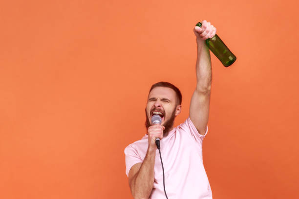 カラオケで時間を過ごし、マイクで歌い、アルコール飲料のボトルで手を挙げる男。 - eastern european caucasian one person alcoholism ストックフォトと画像