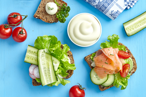 Sandwiches with smoked salmon, cucumber, lettuce, radish and mayo on a blue wooden table, top view