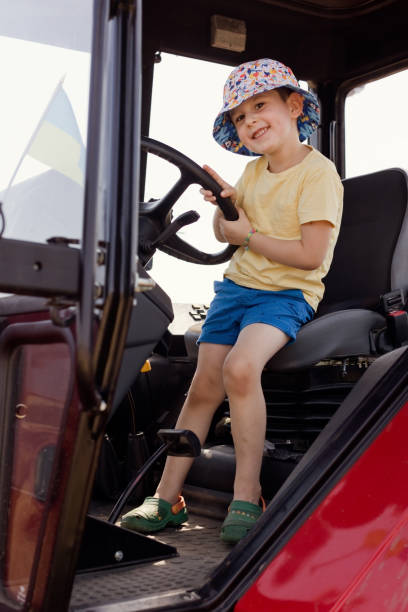 A 10-year-old school-age boy tries to start an old tractor or car. Repair. Little helper. Harvest time. Raising sons by father. Photo. Family farmer. Looking at camera