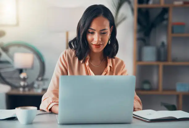Photo of Woman working on laptop online, checking emails and planning on the internet while sitting in an office alone at work. Business woman, corporate professional or manager searching the internet