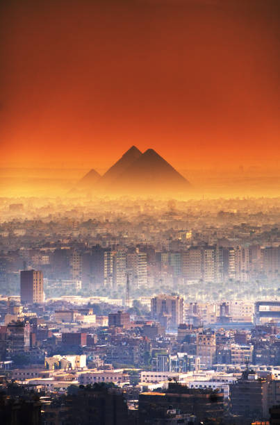 ciel orange spectaculaire au-dessus d’une grande ville du caire avec une vue sur les grandes pyramides de gizeh au loin - pyramid pyramid shape egypt sunset photos et images de collection