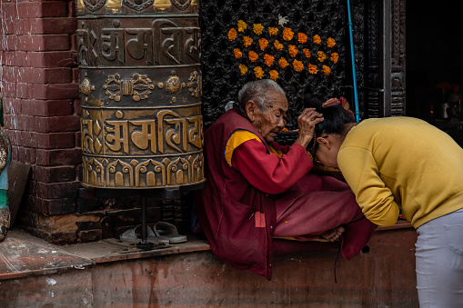 Kathmandu, Nepal - oct 30, 2019: a 100-year-old Tibetan Buddhist nun gives blessings for a fee at the entrance to the Boudhanath stupa, Kathmandu