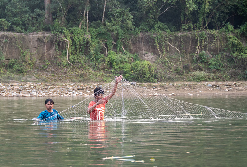 Chitwan N. P . , Nepal - nov 4, 2019:  two young men fishing with nets immersed in the Rapti River, Chitwan N.P., Nepal