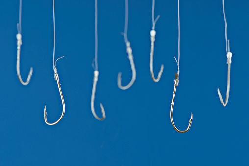 Fishing hooks are hanging with transparent string in front of blue background.