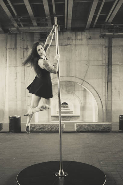 Caucasian middle aged female pole dancer outside White female pole dancer on a stage pole outdoor under a highway overpass with arched supports and lots of concrete. black pole dancers stock pictures, royalty-free photos & images