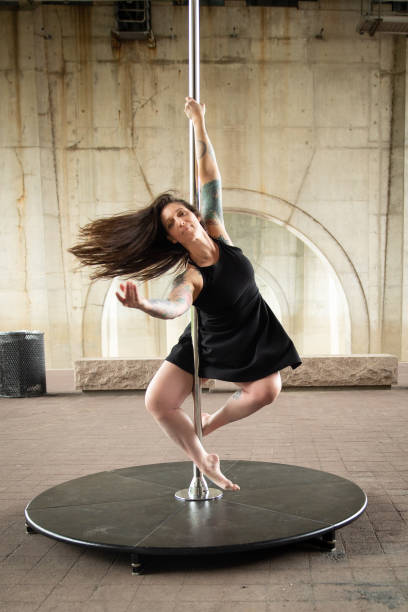 Caucasian middle aged female pole dancer outside White female pole dancer on a stage pole outdoor under a highway overpass with arched supports and lots of concrete. black pole dancers stock pictures, royalty-free photos & images