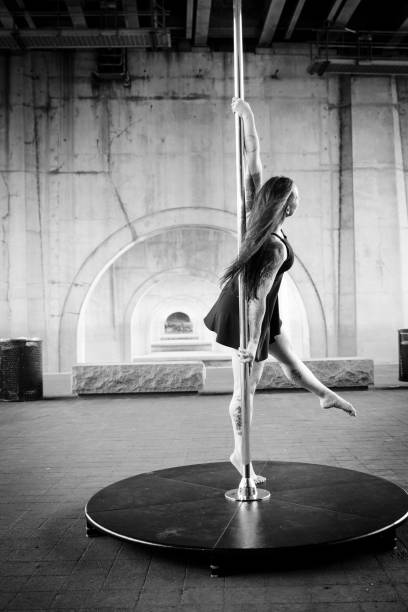 Caucasian middle aged female pole dancer outside White female pole dancer on a stage pole outdoor under a highway overpass with arched supports and lots of concrete. black pole dancers stock pictures, royalty-free photos & images