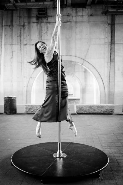 Caucasian middle aged female pole dancer outside White female pole dancer on a stage pole outdoor under a highway overpass with arched supports and lots of concrete. black pole dancers stock pictures, royalty-free photos & images