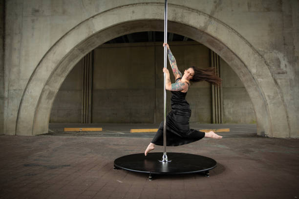 Caucasian middle aged female pole dancer outside White female pole dancer on a stage pole outdoor under a highway overpass with arched supports and lots of concrete. black pole dancers stock pictures, royalty-free photos & images