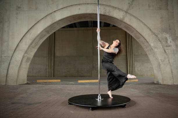 Caucasian middle aged female pole dancer outside White female pole dancer on a stage pole outdoor under a highway overpass with arched supports and lots of concrete. black pole dancers stock pictures, royalty-free photos & images