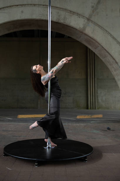 Caucasian middle aged female pole dancer outside White female pole dancer on a stage pole outdoor under a highway overpass with arched supports and lots of concrete. black pole dancers stock pictures, royalty-free photos & images